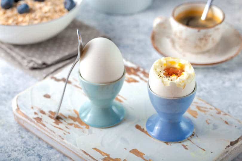 Fresh soft boiled eggs in egg cups in a white concrete rustic background